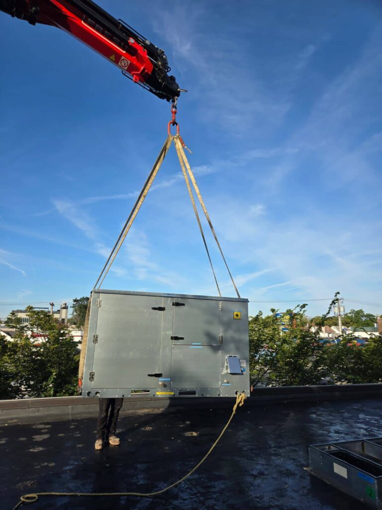 Rooftop HVAC unit suspended from a crane above a New York building